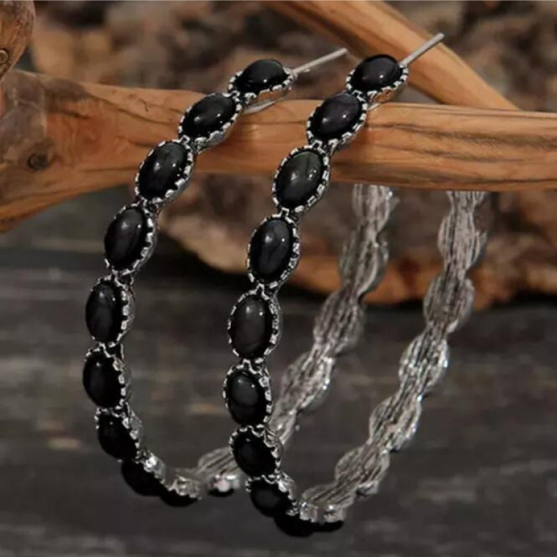 Pair of curved C-hoop earrings feature elongated black oval accents framed by silver-toned alloy detailing in a statement silhouette.