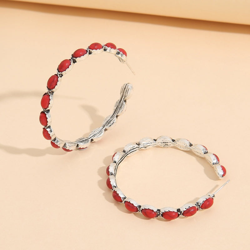 Silver-tone C-hoop earrings feature a large open silhouette, textured twisted construction, and repeated red oval stone accents around the curve.