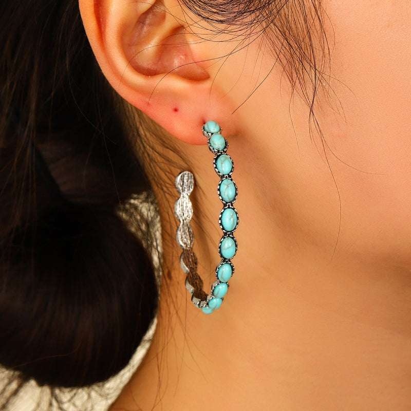 Close-up of a model wearing an artificial turquoise C-hoop earring with a curved silhouette and oval stones set in a textured alloy frame.