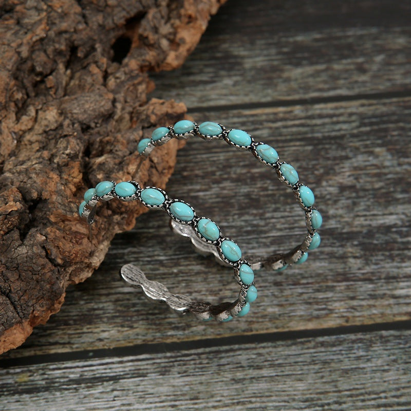 Pair of alloy C-hoop earrings feature curved silhouettes lined with oval artificial turquoise stones in a textured silver-tone setting.
