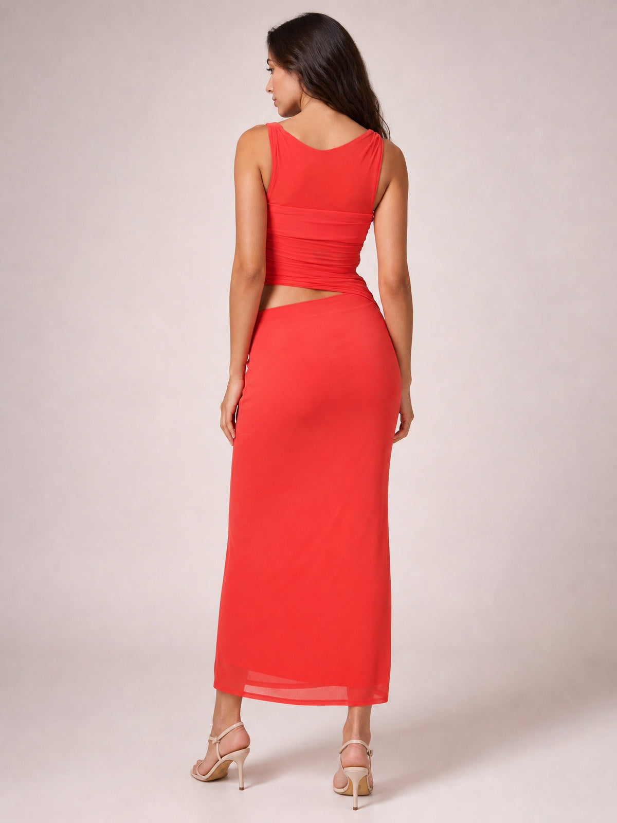 Model viewed from the back in a bright red asymmetrical cutout sleeveless maxi dress with twisted ruching, fitted waist, and ankle-length skirt.