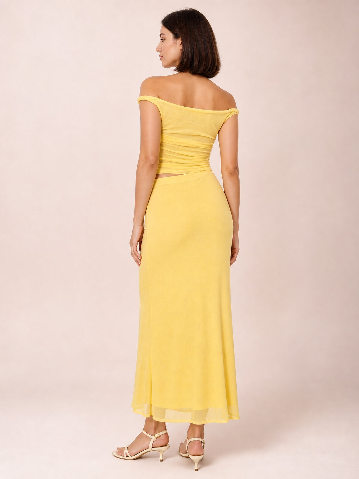 A model poses turned away in a yellow asymmetrical cutout sleeveless dress with twisted ruching, a waist cutout, and a flowing figure-skimming maxi skirt.