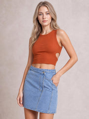 A model poses with one hand in the pocket of a light-wash denim mini skirt featuring button details, stitched panels, and an asymmetrical hem.