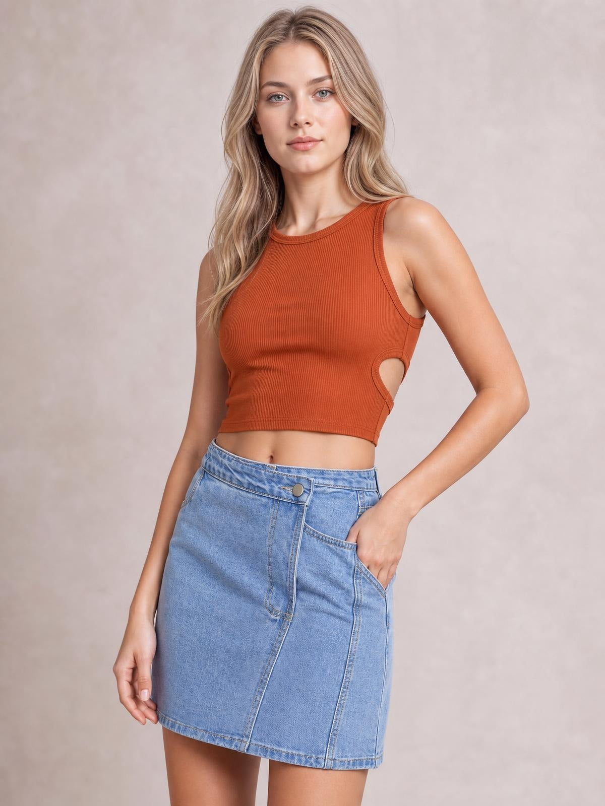 A model poses with one hand in the pocket of a light-wash denim mini skirt featuring button details, stitched panels, and an asymmetrical hem.