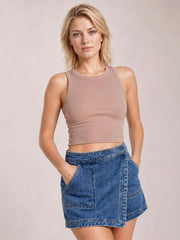 Model poses with hands in the pockets of a blue denim skort featuring an asymmetrical front, high waist, contrast stitching, and structured panel construction.
