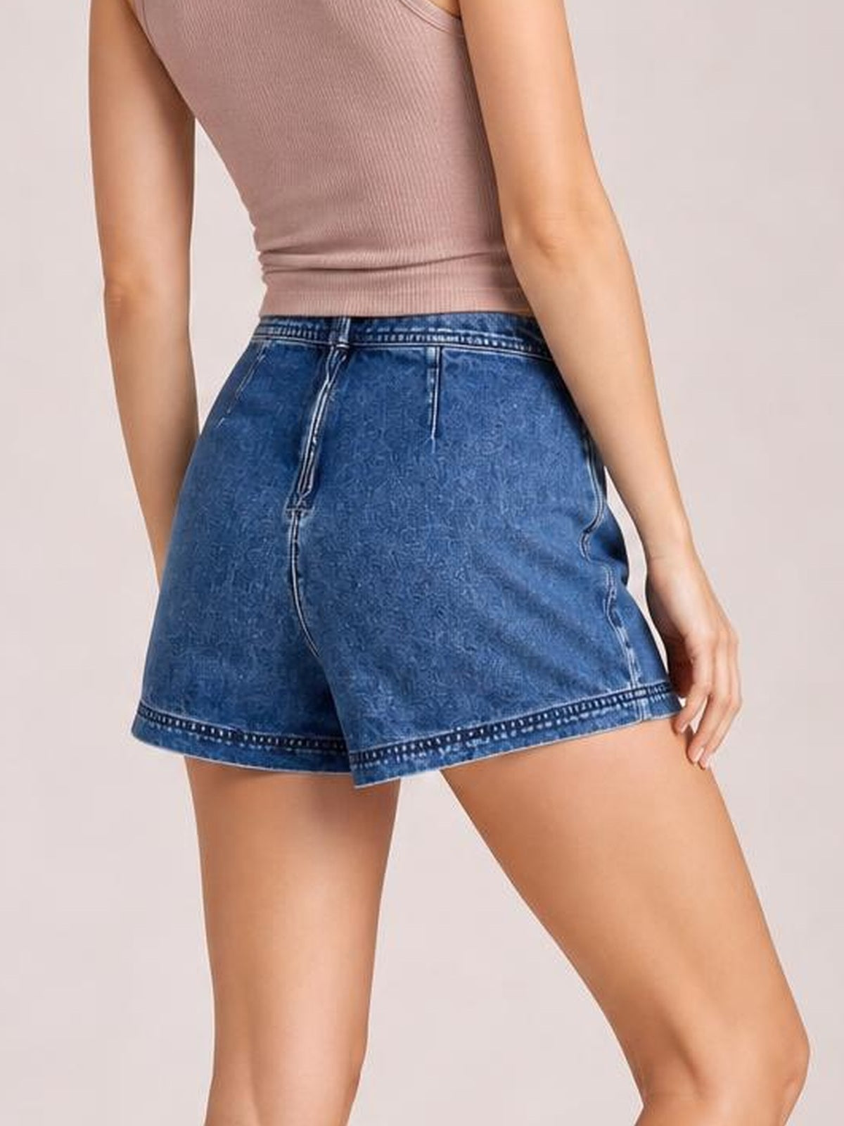 A model wears a blue denim skort with an asymmetrical overlapping hem, high waistband, front zipper, visible pockets, and a relaxed A-line silhouette.