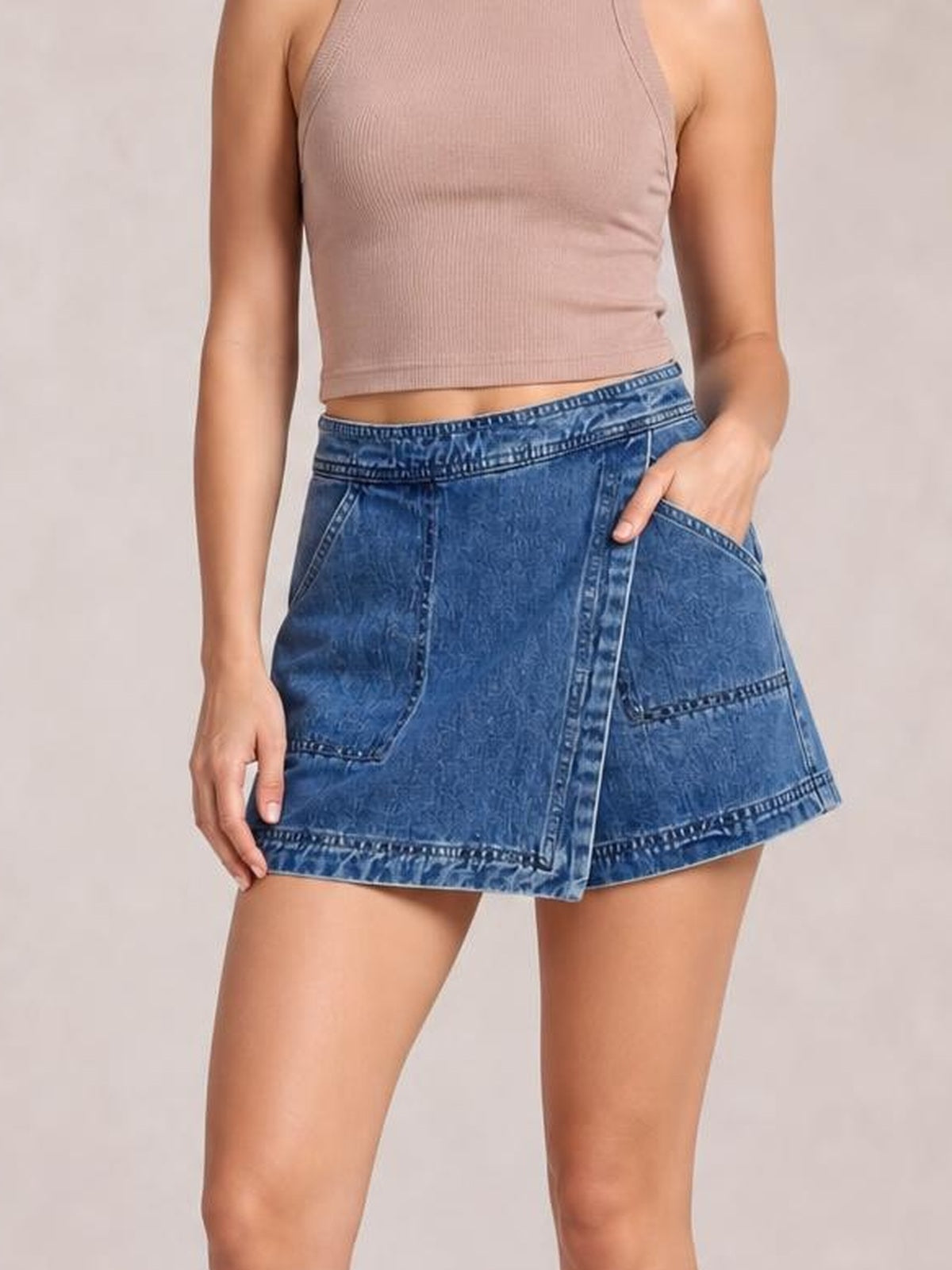 A model wears a blue asymmetrical denim skort with an elasticized waistband, roomy pockets, stitched panel details, and a relaxed short silhouette.