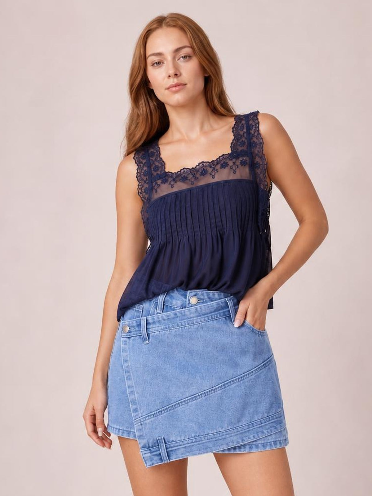 Model poses with one hand in a pocket, showcasing a light-blue denim skort with an asymmetrical wrap-style front, diagonal seaming, and visible shorts underneath.