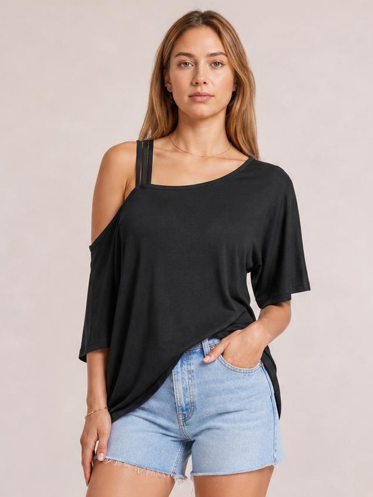 Model poses in a black asymmetrical neck half sleeve T-shirt with a relaxed oversized silhouette and exposed left shoulder.