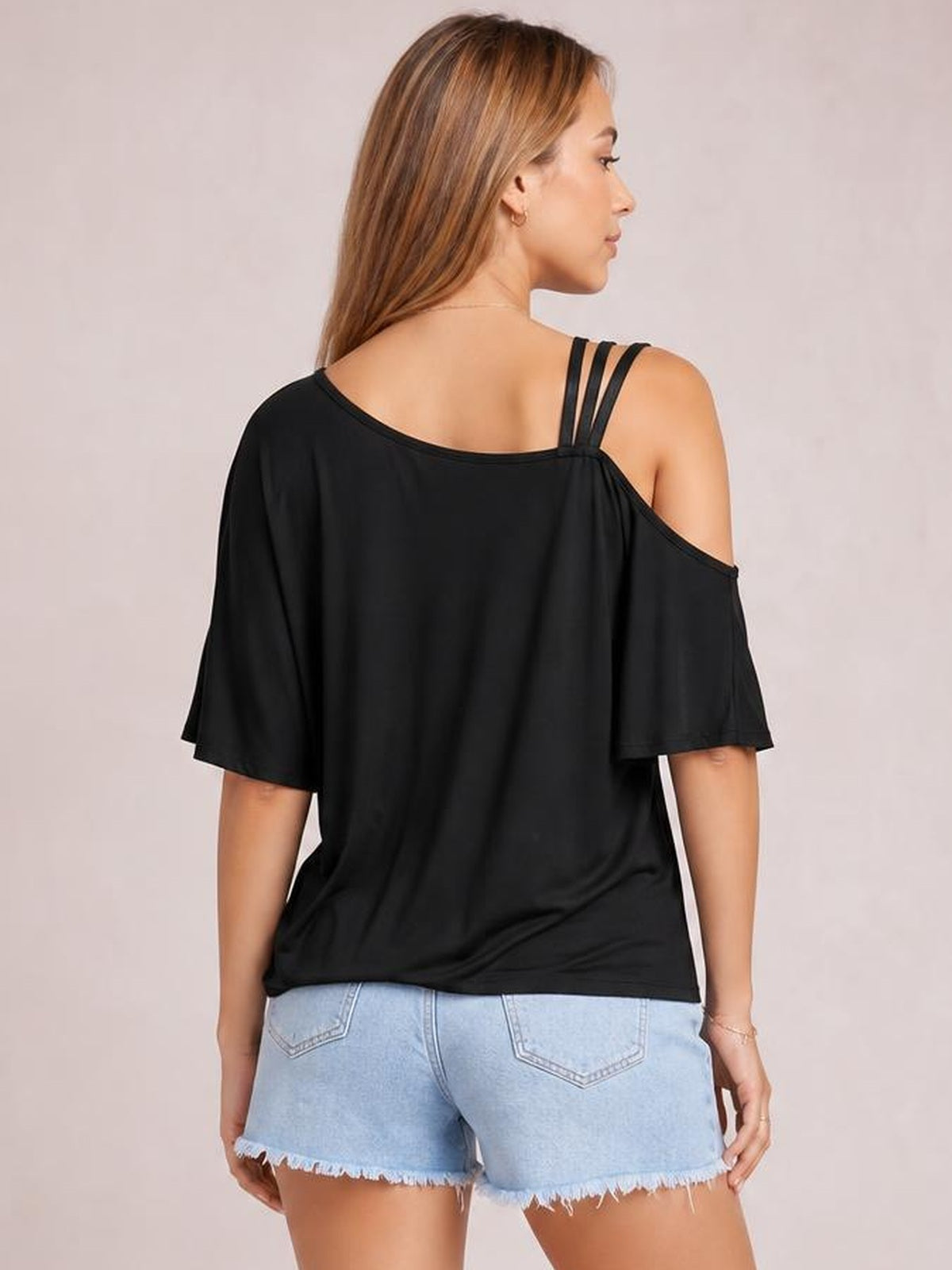 Model viewed from behind wearing a black asymmetrical neck half sleeve T-shirt with a relaxed draped silhouette and exposed shoulder detail.