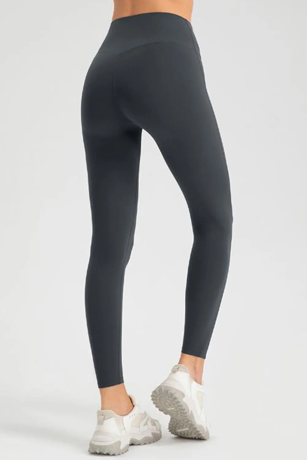 Model in a turned pose wears black high-waist skinny active pants with a sleek, stretchy full-length legging silhouette and fitted construction.