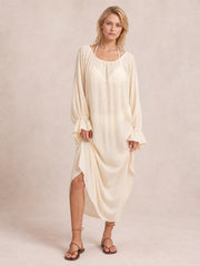 A model stands in a cream cover-up with a loose, flowing silhouette, scoop neckline, long sleeves, and gathered flounce cuffs.
