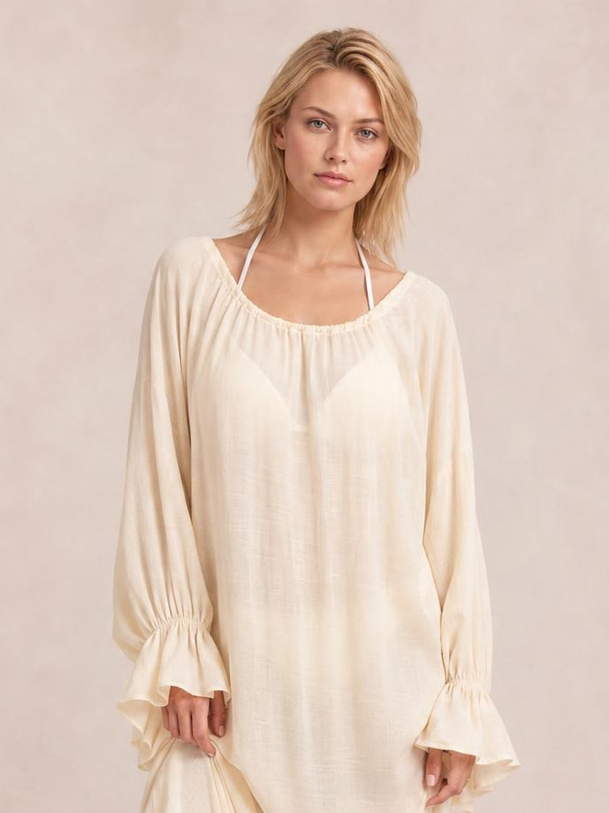 A model stands in a cream cover-up with a loose silhouette, gathered scoop neckline, and long flounce sleeves with elasticated cuffs.