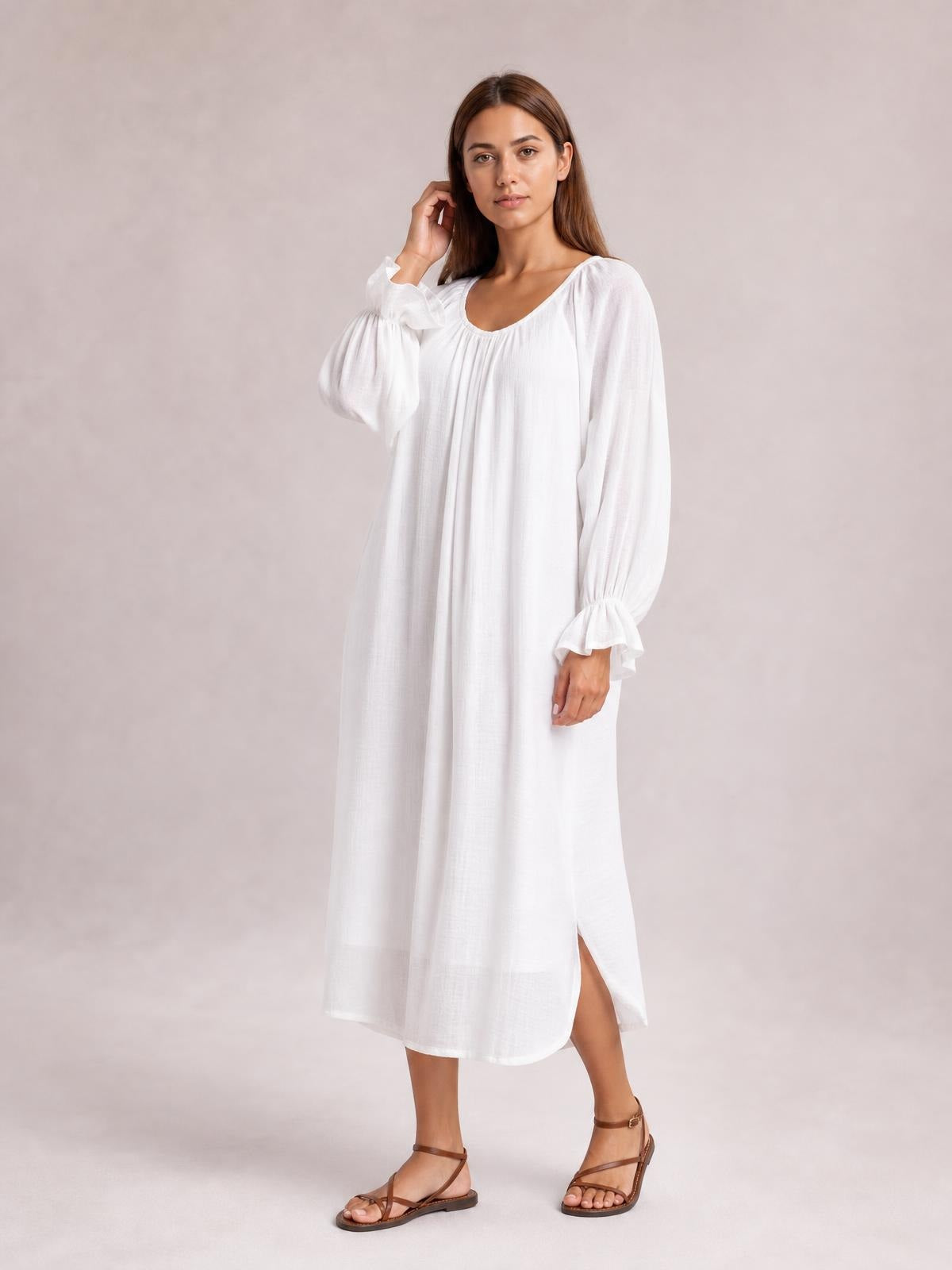 A model poses in a white backless cover-up with a loose midi silhouette, scoop neckline, long flounce sleeves, and gathered cuffs.