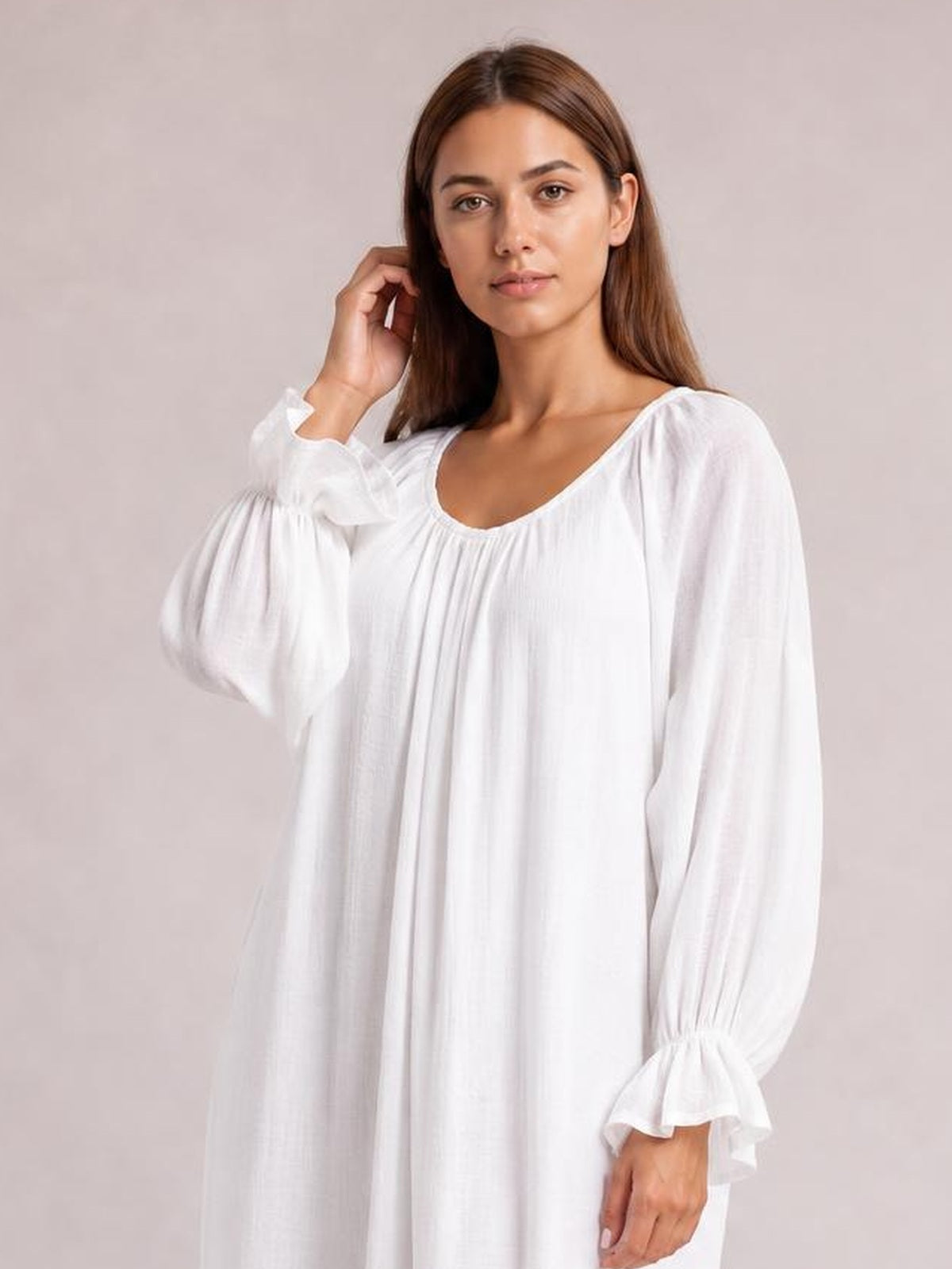 A woman models a white cover-up with a loose, flowing silhouette, gathered scoop neckline, voluminous long sleeves, and flounce cuffs while touching her hair.