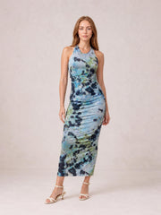 Model poses in a blue, green, and black printed halter neck dress with a fitted ruched silhouette and midi-length hem.