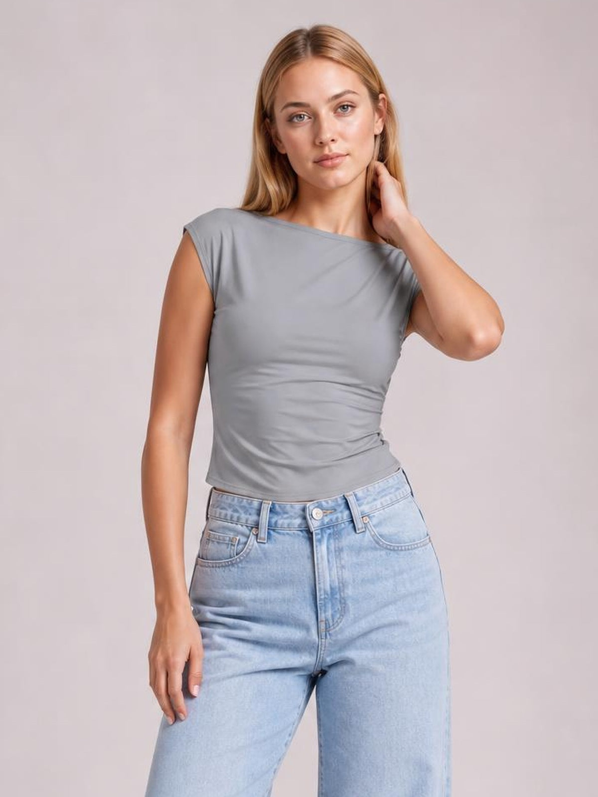 A model wears a solid gray cropped blouse with a wide round neckline, short sleeves, and a fitted, softly ruched silhouette, touching her neck.