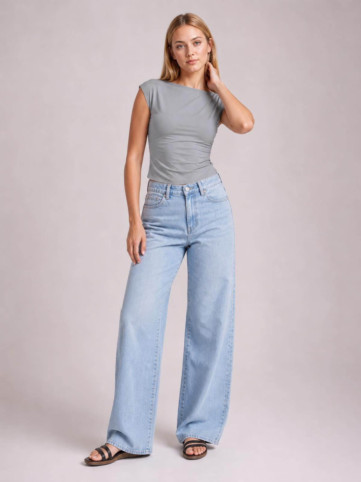 A model poses in a solid gray cropped blouse with a round neck, short regular sleeves, and a fitted silhouette, touching her hair with one hand.