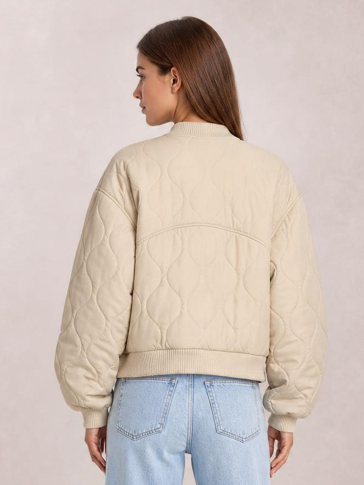 Model shown from behind wearing a cream quilted baseball collar jacket with long sleeves, ribbed cuffs and hem, and a relaxed cropped silhouette.