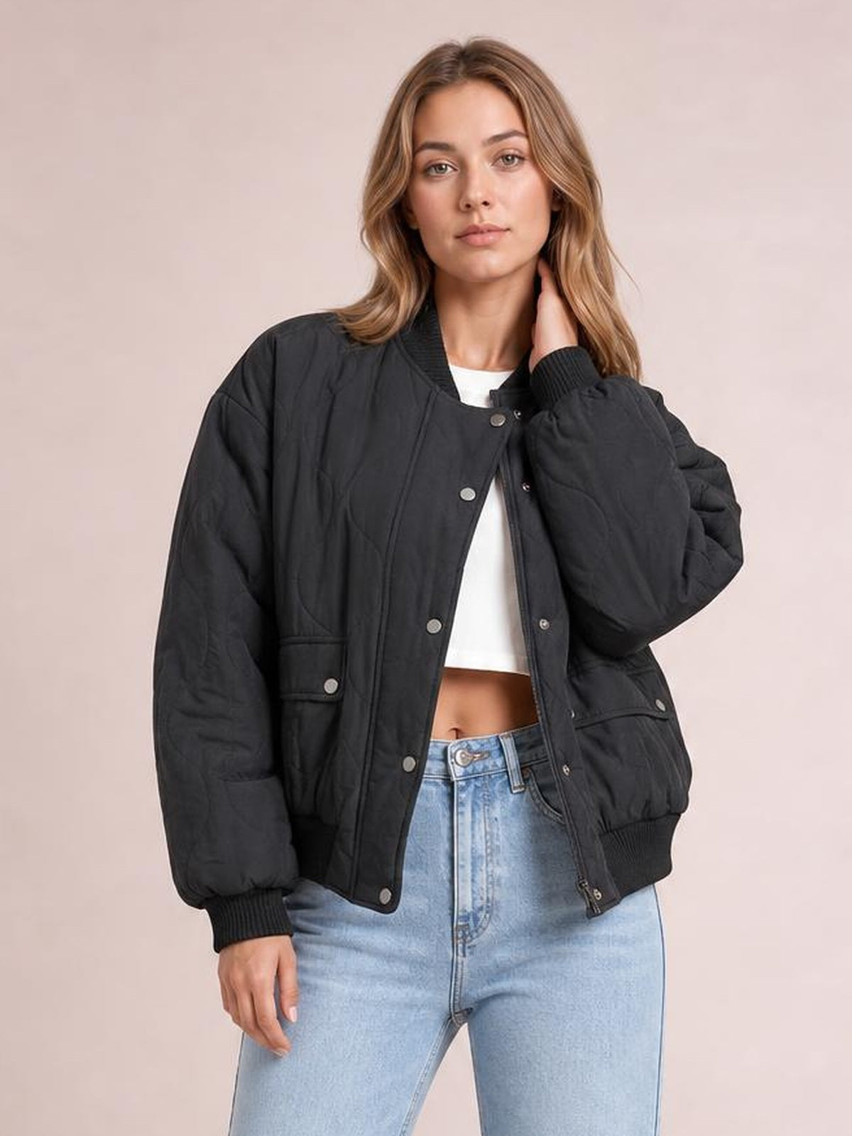 Model poses in a black baseball collar snap-down long sleeve jacket with a relaxed silhouette, ribbed cuffs and hem, and front flap pockets.