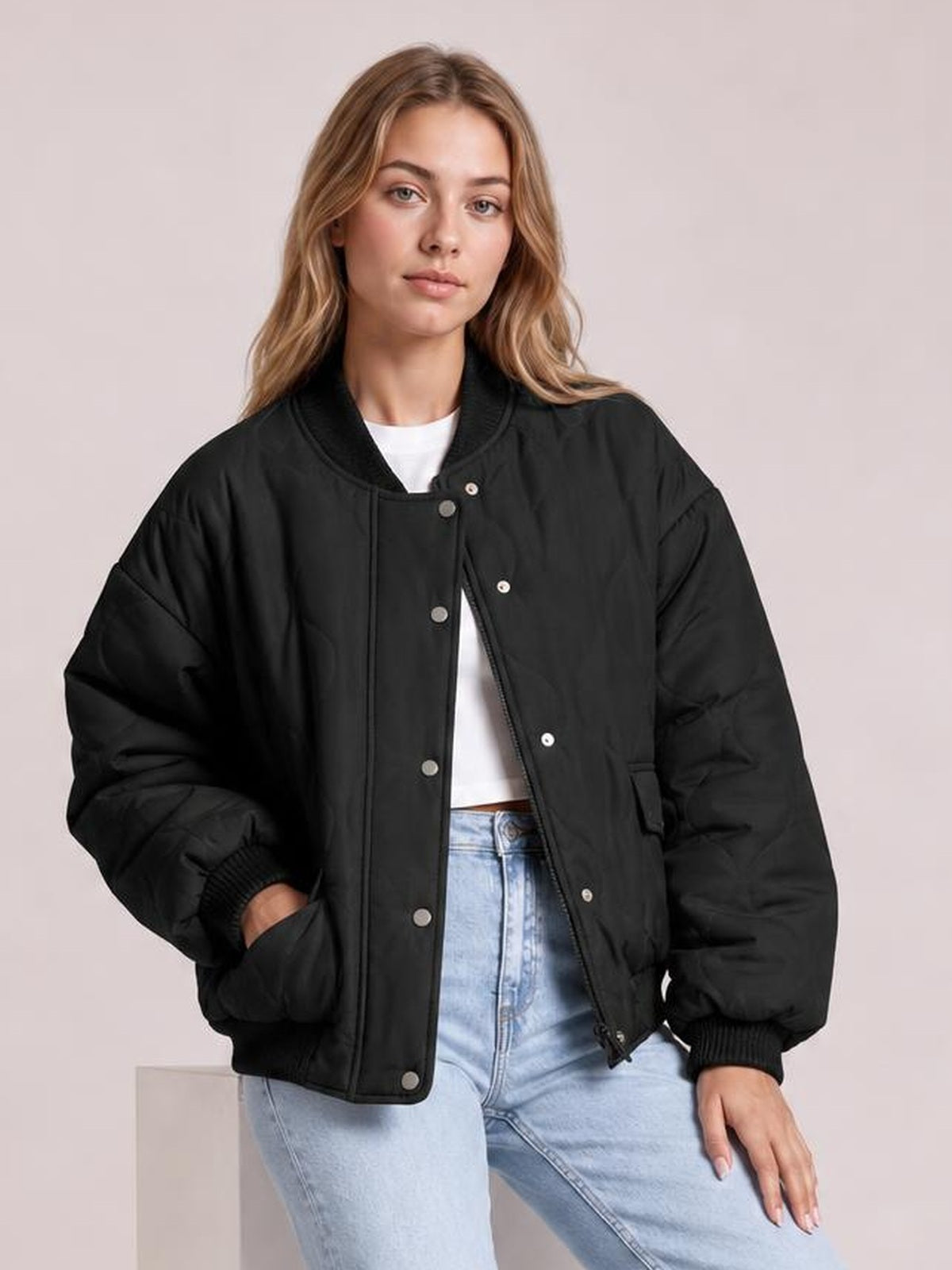 Model wears a black baseball collar snap-down long sleeve jacket with a relaxed silhouette, ribbed cuffs, and side pockets, posing with one hand tucked in.