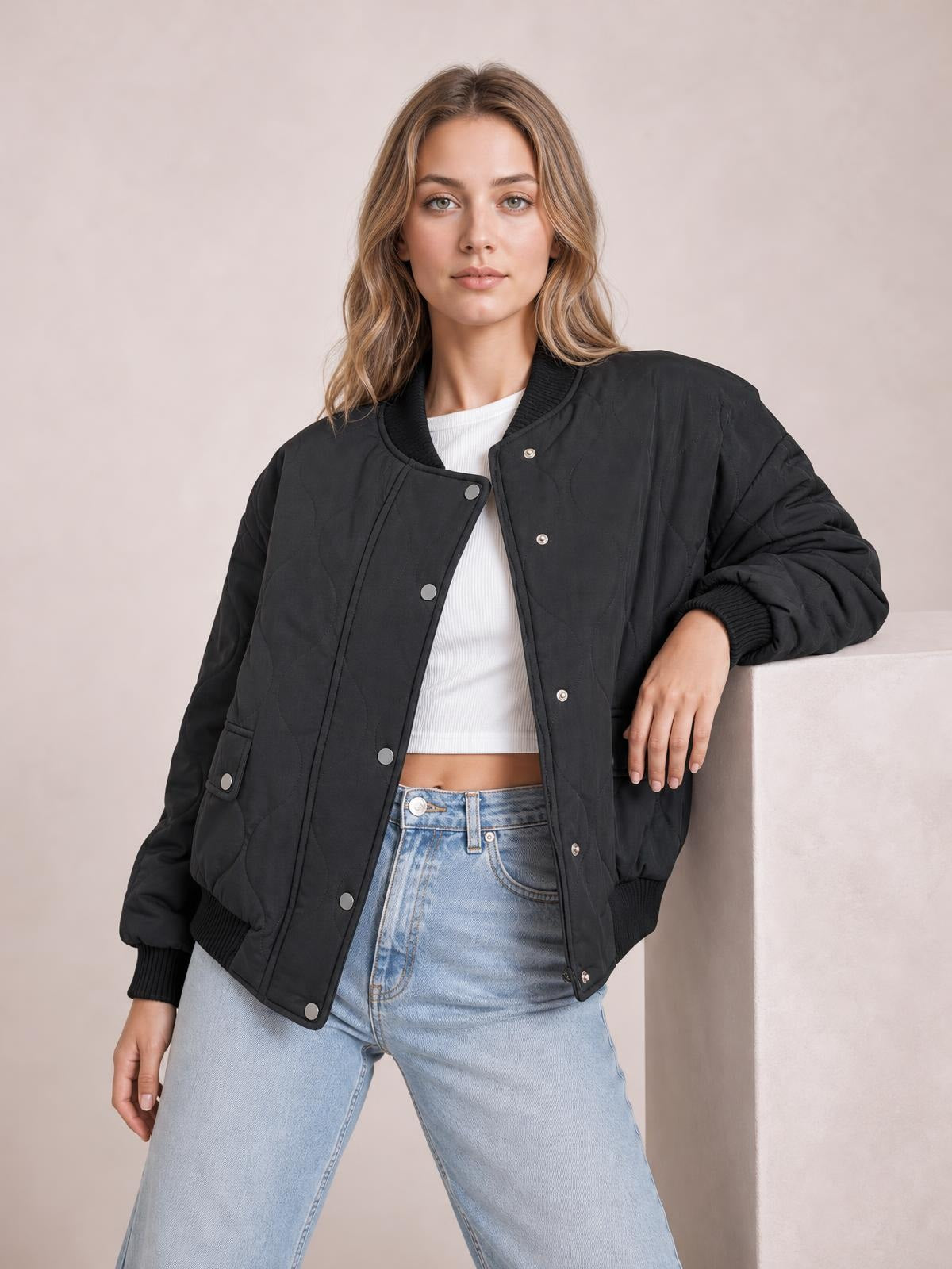 A model poses in a black baseball-collar snap-down long-sleeve jacket with a relaxed silhouette, ribbed cuffs and hem, front pockets, and quilted stitching.