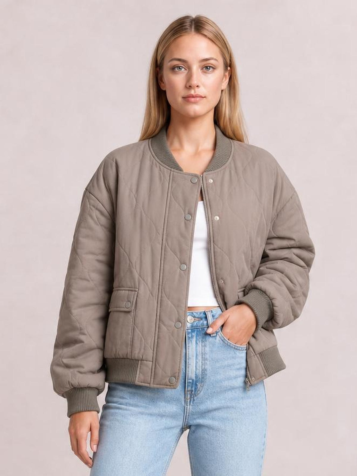 A model wears a taupe quilted baseball collar snap-down long sleeve jacket with ribbed cuffs and hem, patch pockets, and a relaxed silhouette.