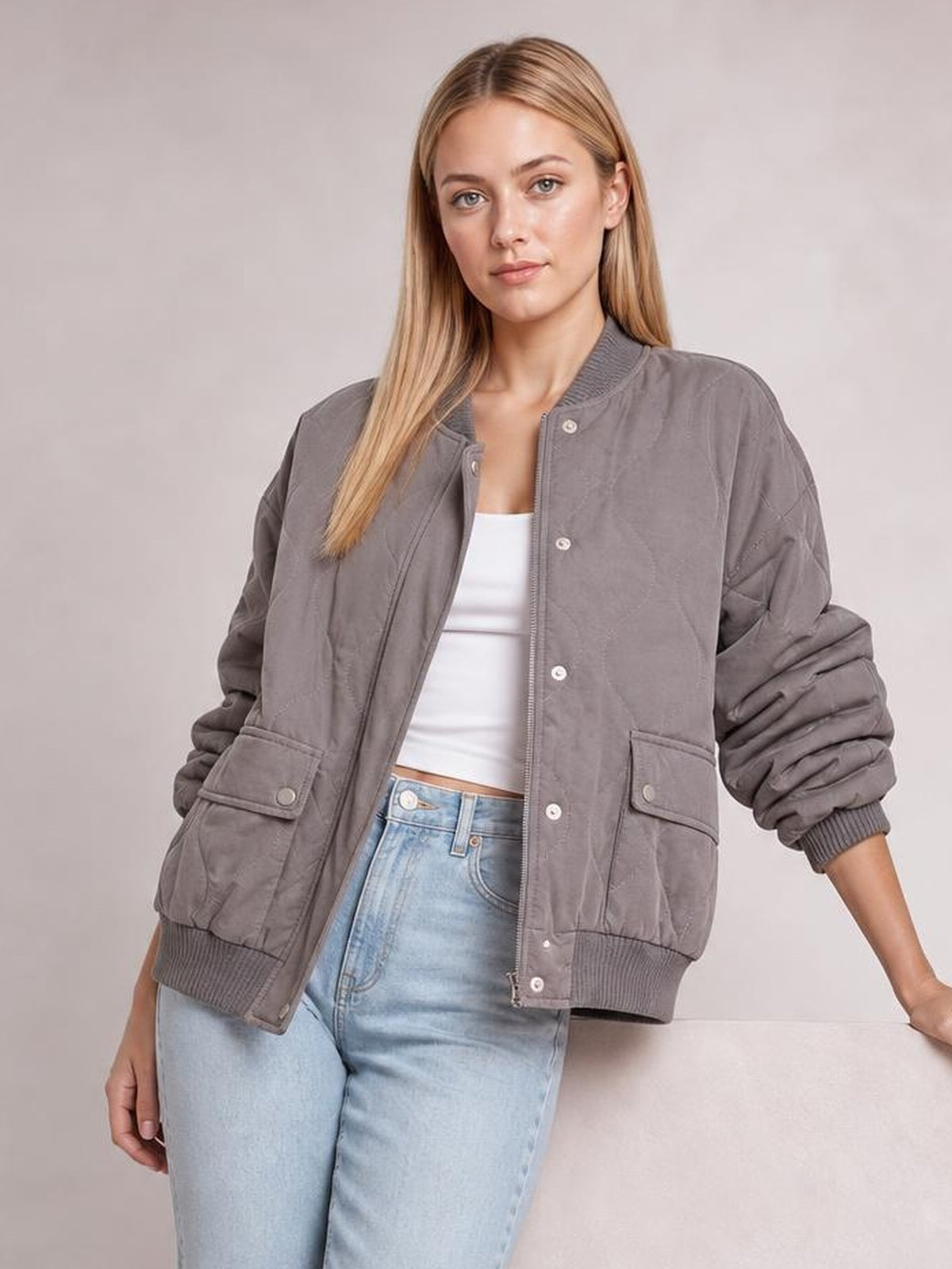 Model wears a gray baseball-collar snap-down jacket with long sleeves, ribbed cuffs and hem, flap pockets, and a relaxed silhouette, standing with one arm extended.