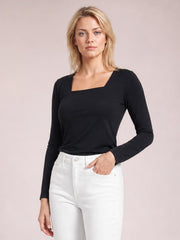 Model poses with one hand in her pocket wearing a fitted black asymmetrical-neck long-sleeve top with a clean, opaque silhouette.
