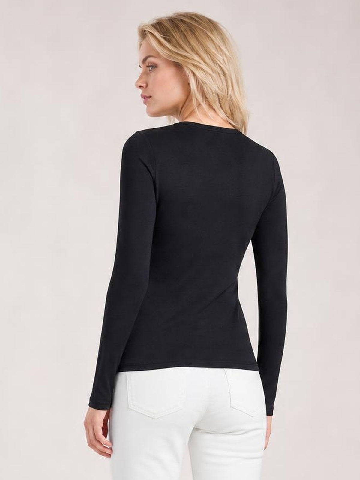 Model turns to show the back of a black asymmetrical neck long sleeve top with a smooth, fitted silhouette and straight hem.