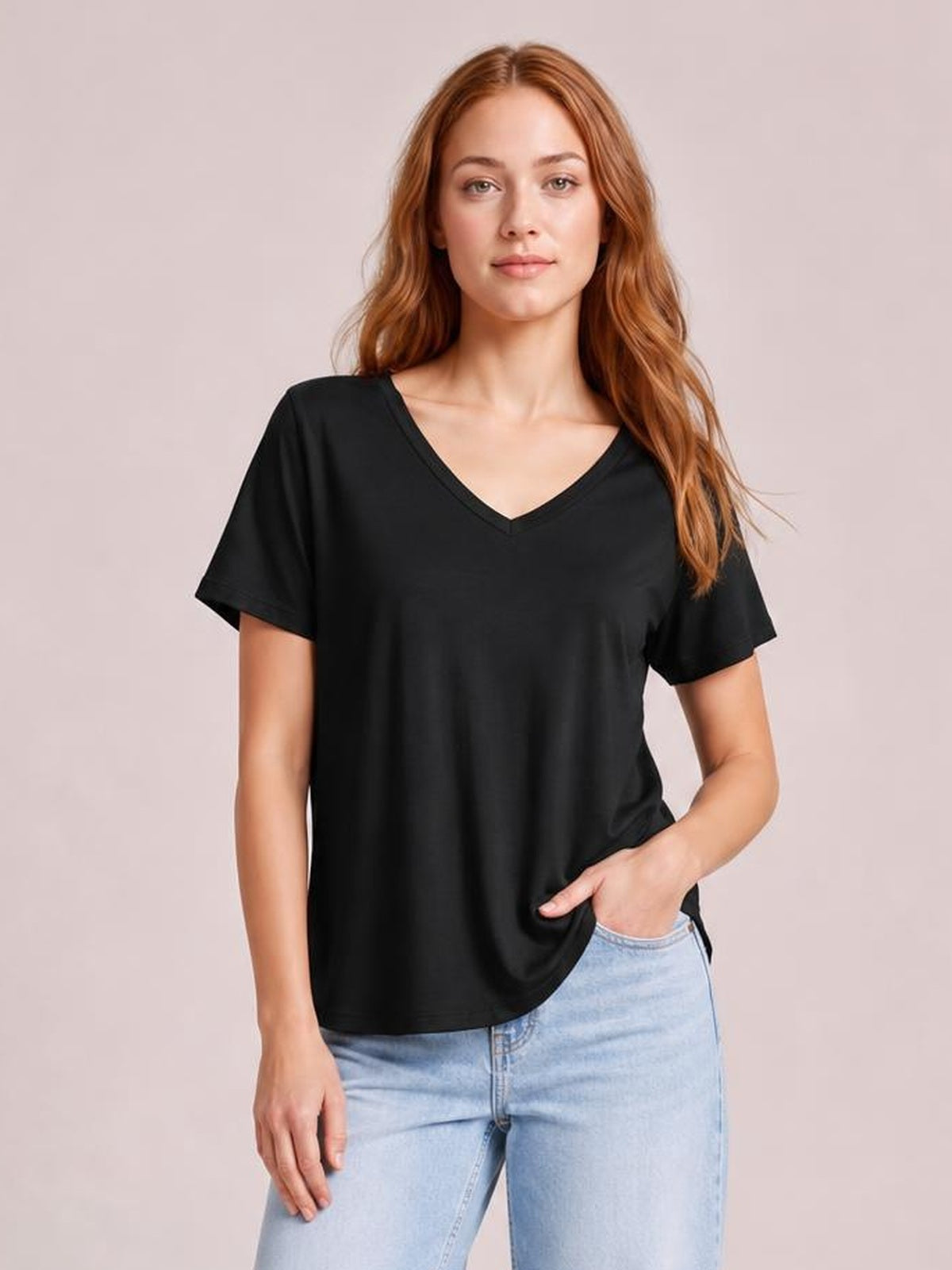 Model wearing a black bamboo V-neck T-shirt with short sleeves, a relaxed silhouette, and a slightly longer curved high-low hem, posed with one hand in her jeans pocket.
