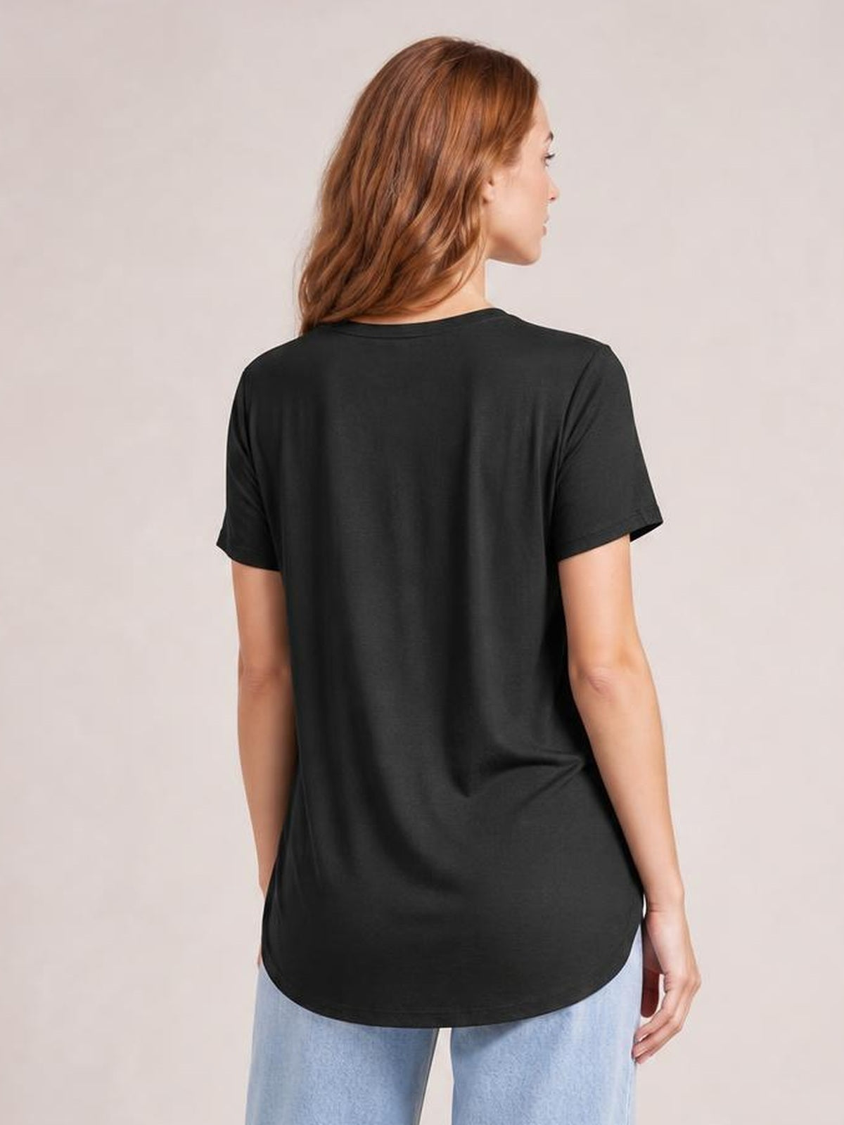 Model shown from the back in a black bamboo T-shirt with short sleeves, a relaxed silhouette, smooth construction, and a rounded high-low hem.