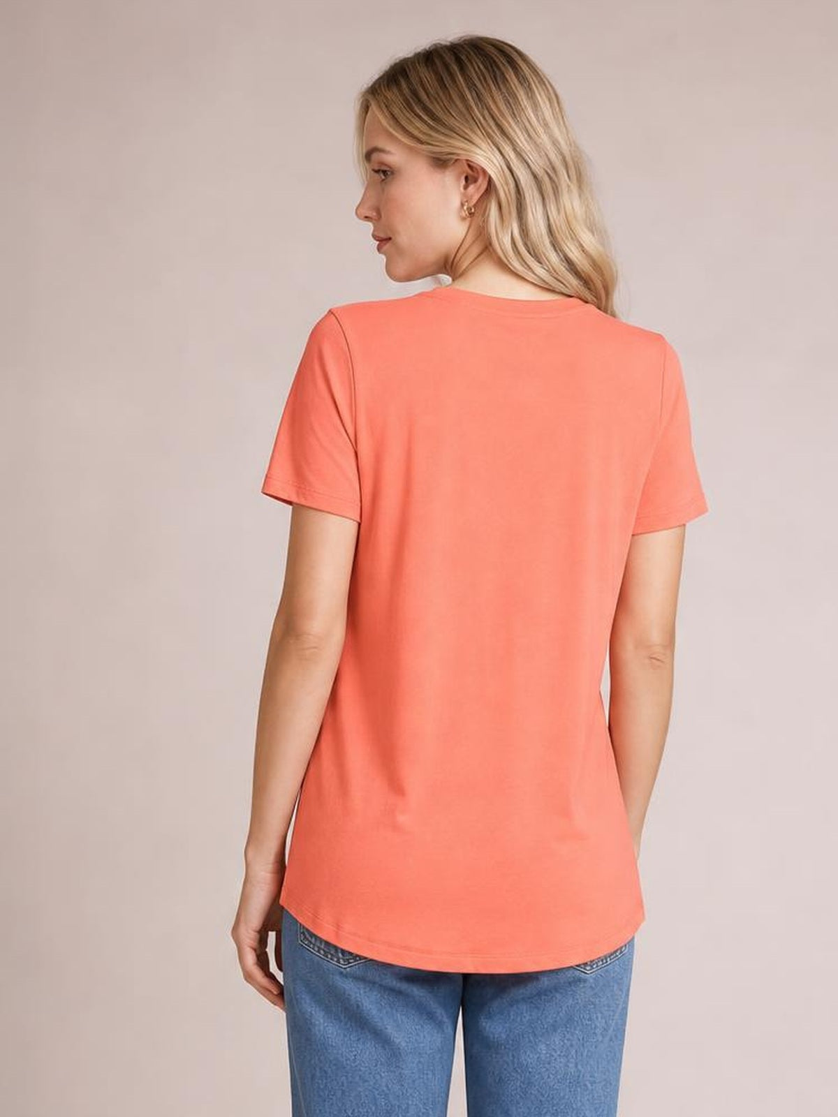 A model shows the back of a coral bamboo-blend T-shirt with short sleeves, a relaxed silhouette, and a curved high-low hem.