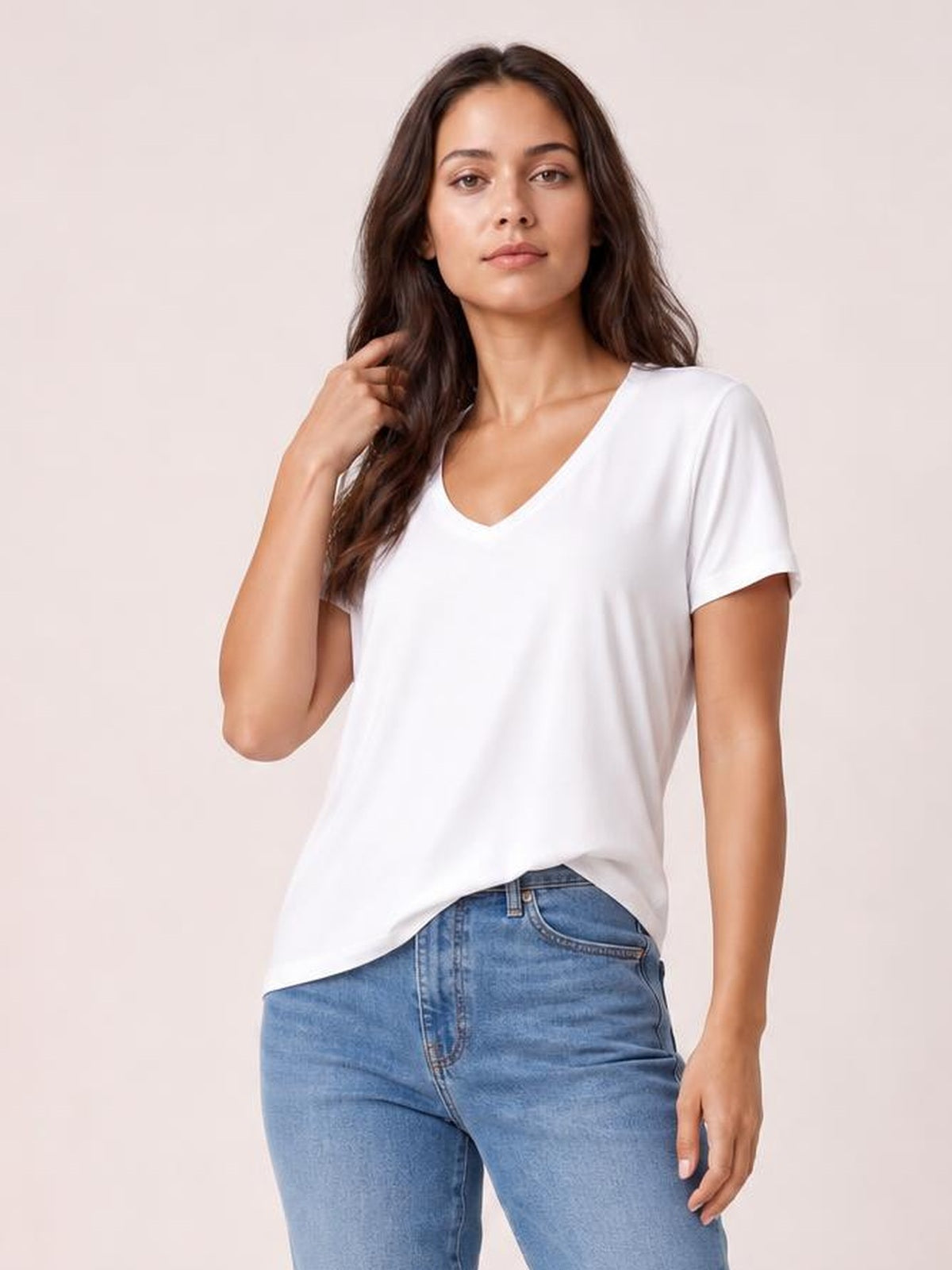 Model wearing a white bamboo V-neck T-shirt with short sleeves, a relaxed high-low hem, and a slightly loose silhouette while touching her hair.