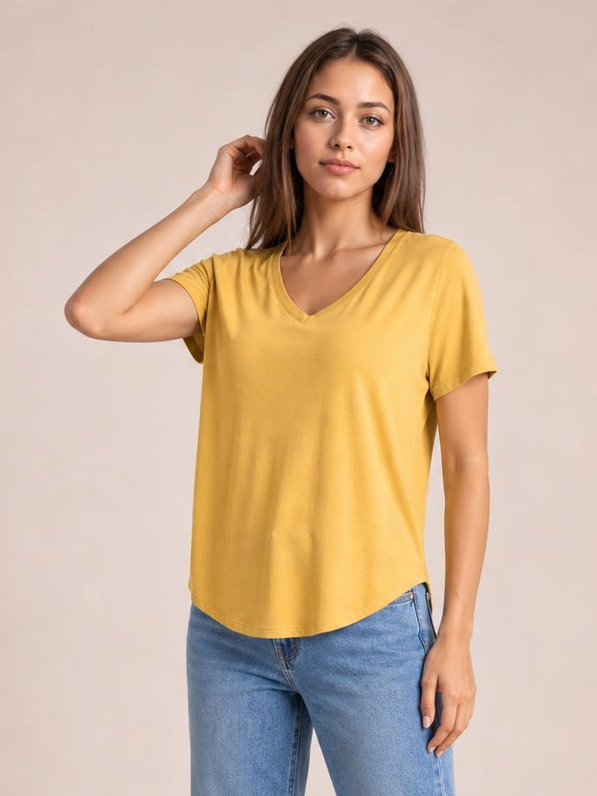 A model poses in a mustard-yellow bamboo V-neck T-shirt with short sleeves, a relaxed silhouette, and a curved high-low hem.