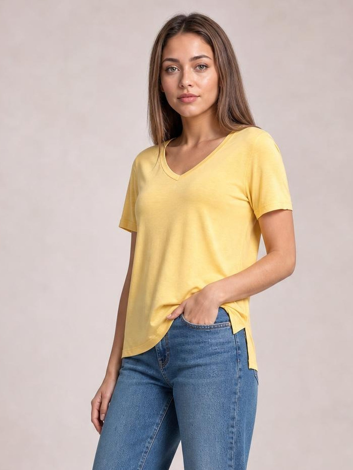 Model wears a sunny yellow bamboo V-neck T-shirt with short sleeves, relaxed silhouette, and a curved high-low hem over blue jeans.
