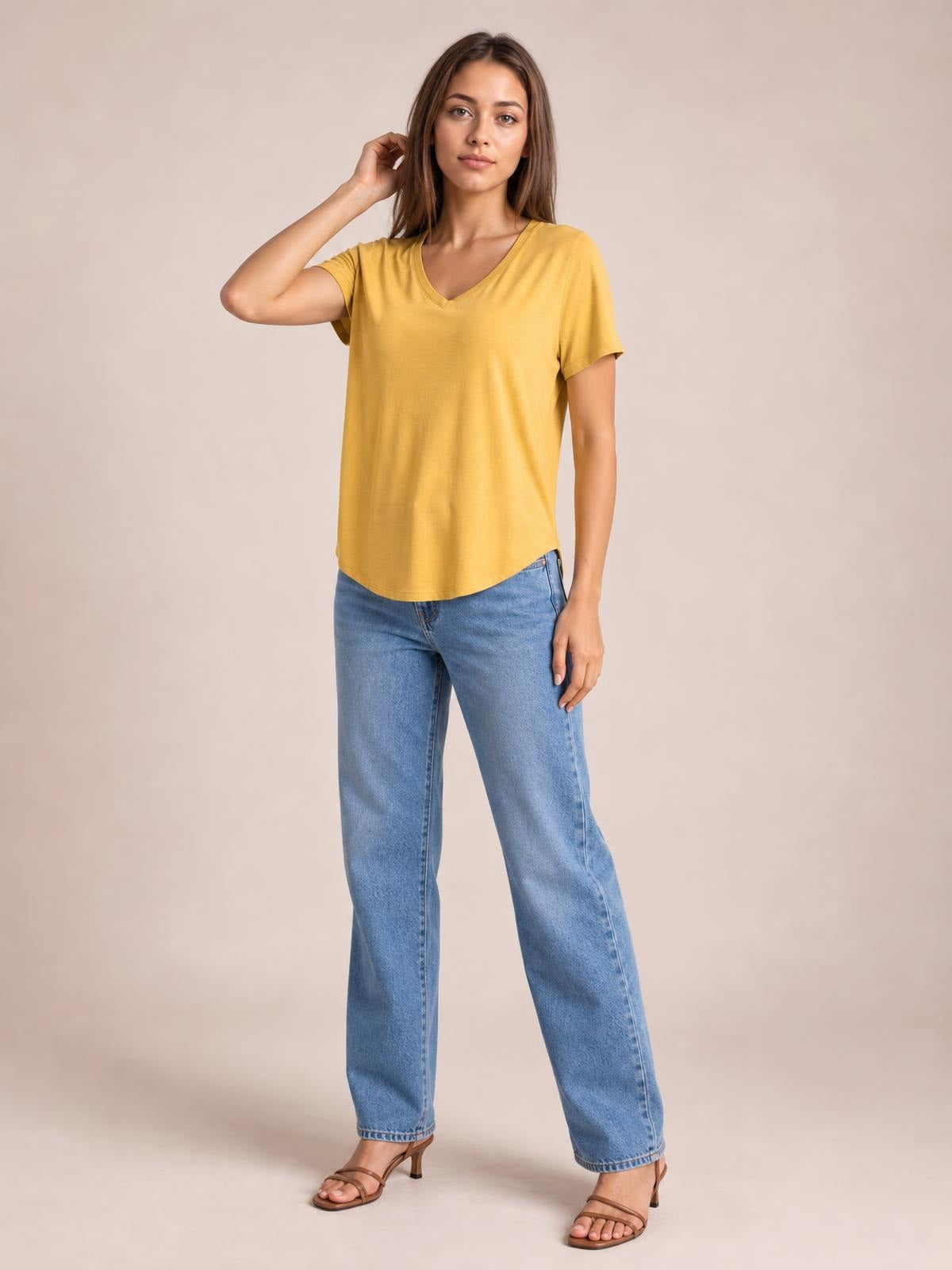 A woman poses in a mustard-yellow bamboo V-neck T-shirt with short sleeves, a relaxed silhouette, and a rounded high-low hem.
