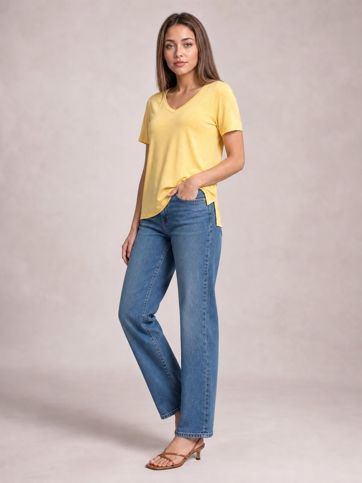 Woman wearing a yellow bamboo V-neck high-low T-shirt with short sleeves and a relaxed silhouette, posing with one hand in her jeans pocket.