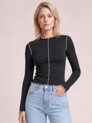 Model poses in a black stretchy mock neck long sleeve T-shirt with contrast trim, fitted silhouette, center seam, and scalloped edges.