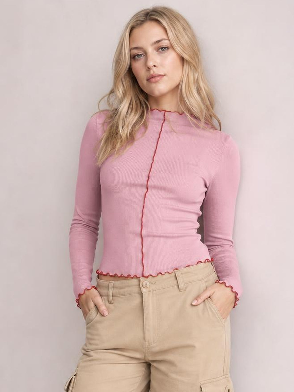 Model wearing a fitted pink mock neck long sleeve T-shirt with contrasting red trim at the neckline, center seam, cuffs, and hem.