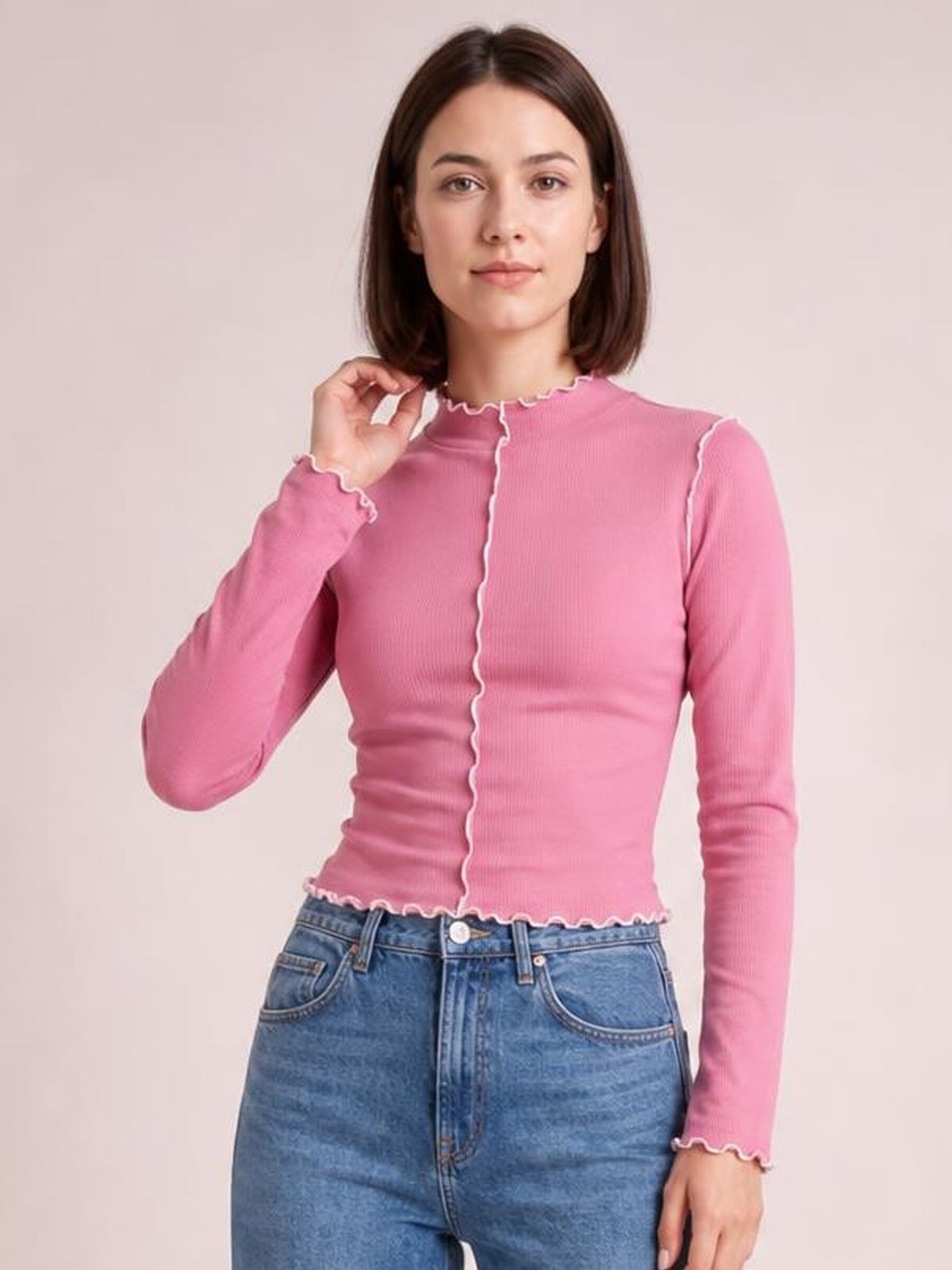 A model poses in a fitted pink mock neck long sleeve T-shirt with white contrast trim, scalloped edges, and a stretchy ribbed silhouette.