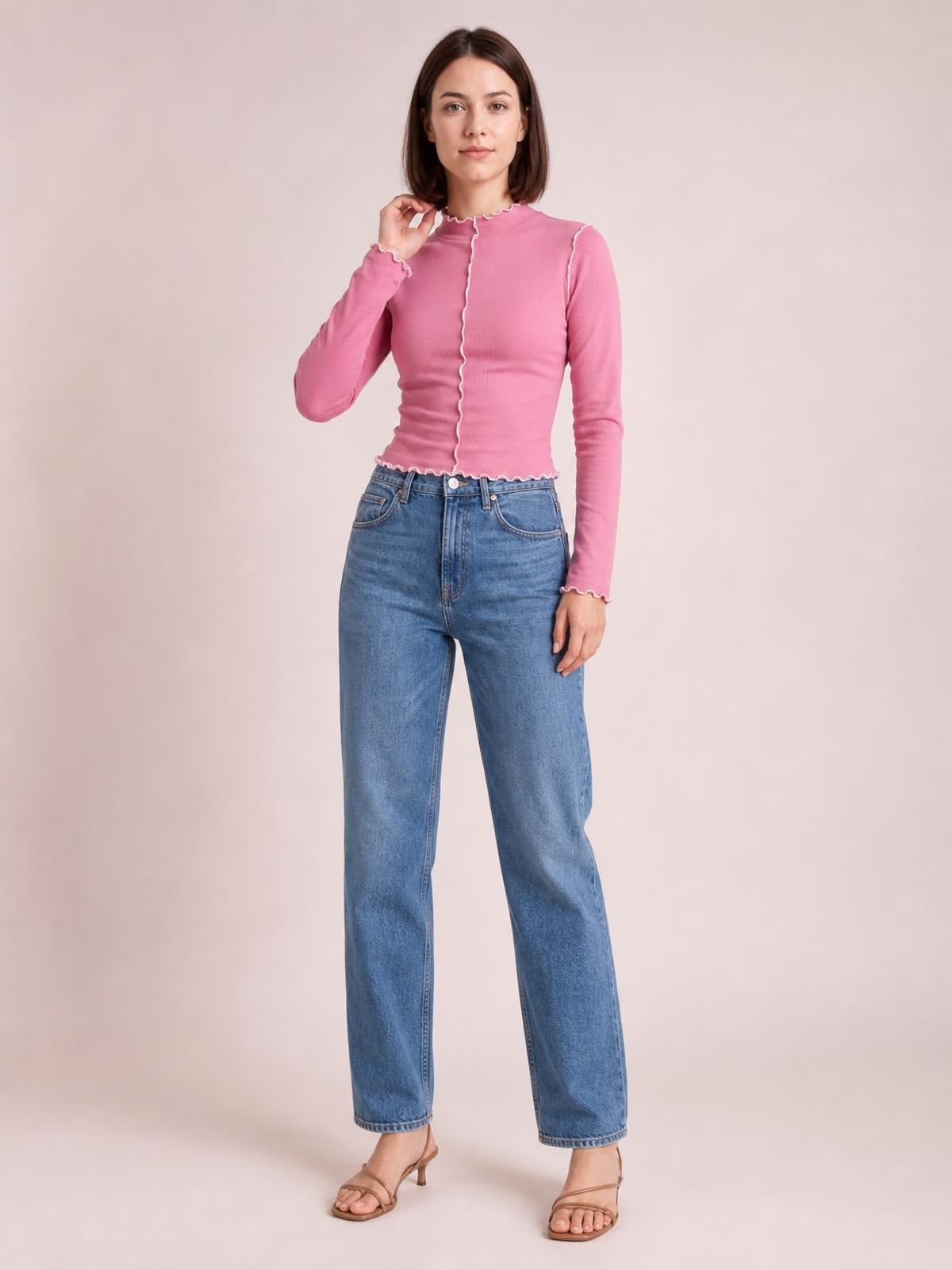 A model poses in a fitted pink mock neck long sleeve T-shirt with contrasting white scalloped trim along the collar, center seam, cuffs, and hem.
