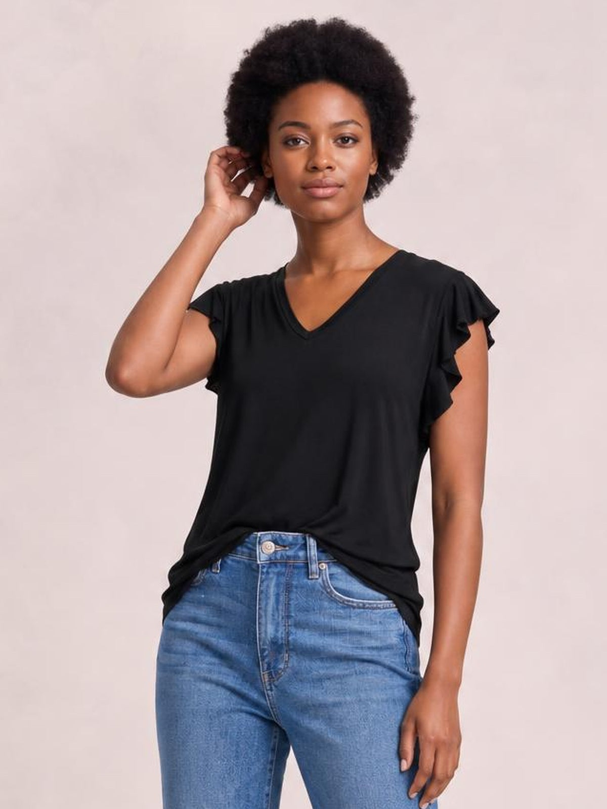 Model wearing a black bamboo notched T-shirt with a relaxed silhouette, V-neckline, and layered ruffled short sleeves, posing with one hand near her hair.