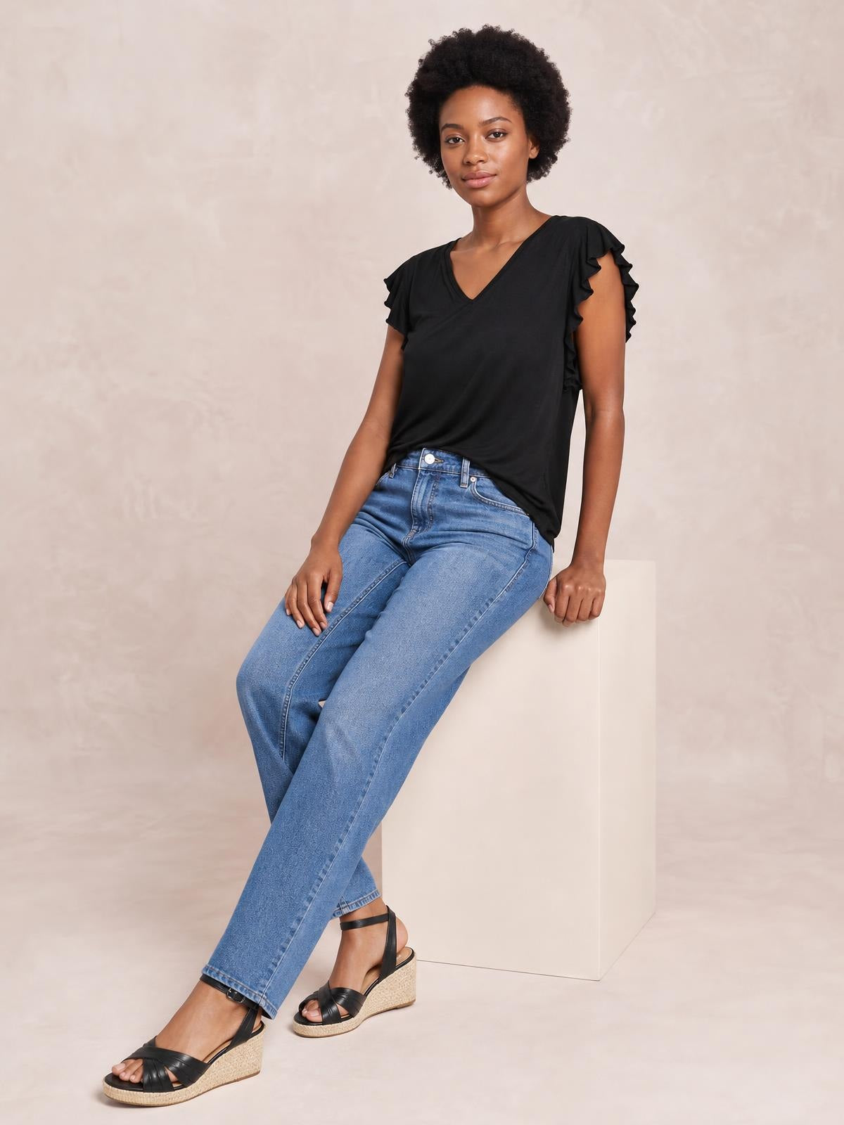 Model seated in a black bamboo notched short sleeve T-shirt with ruffled sleeves and a relaxed silhouette.