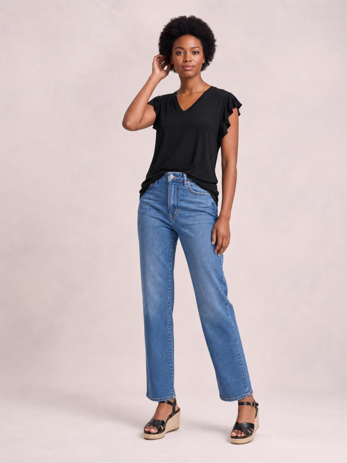 Model wearing a black bamboo notched T-shirt with a V neckline, ruffled short sleeves, and a relaxed stretchy silhouette, posing with one hand near her hair.