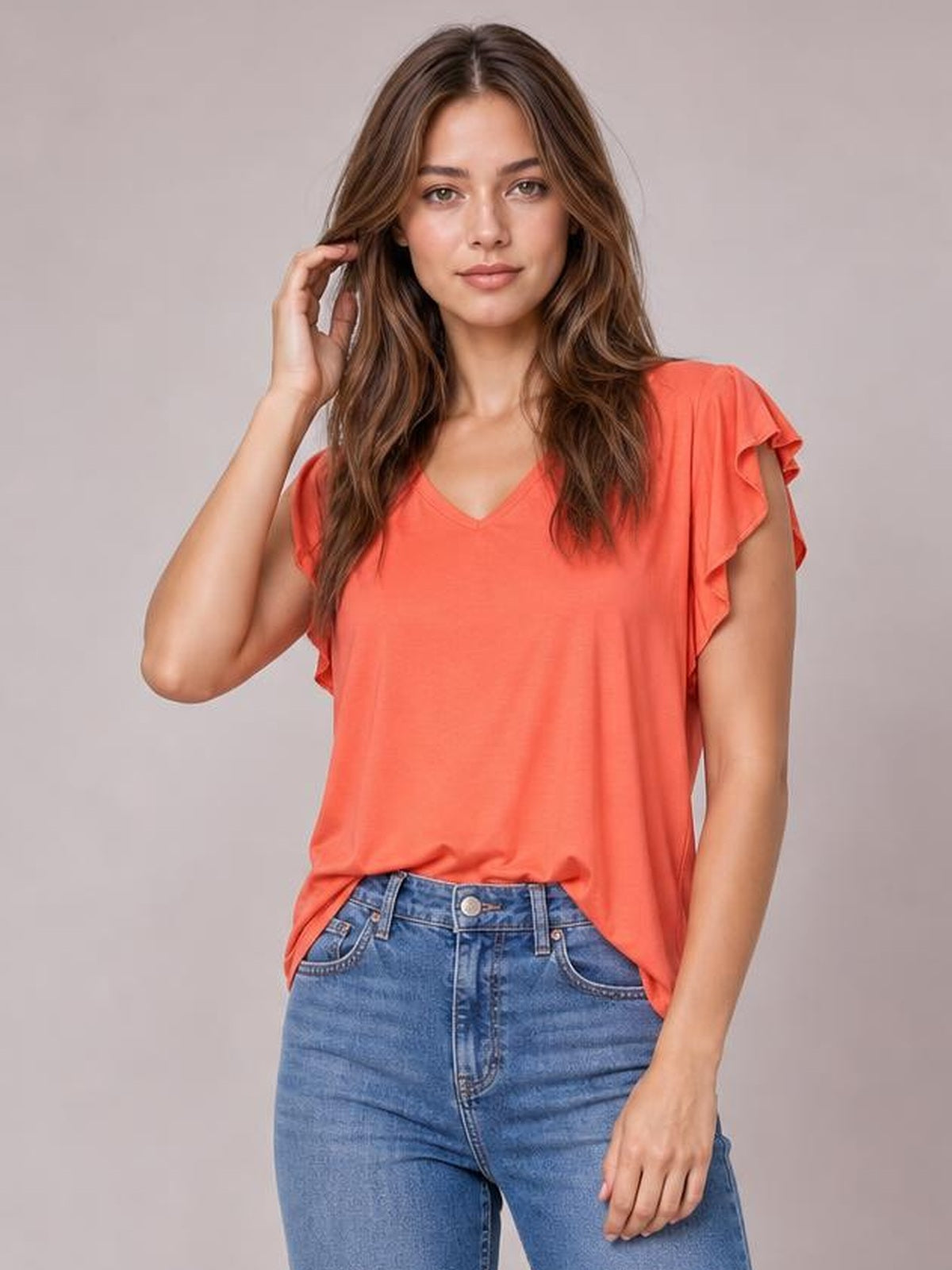 Model wears a coral bamboo T-shirt with a notched neckline, ruffled short sleeves, and a relaxed straight silhouette while touching her hair.
