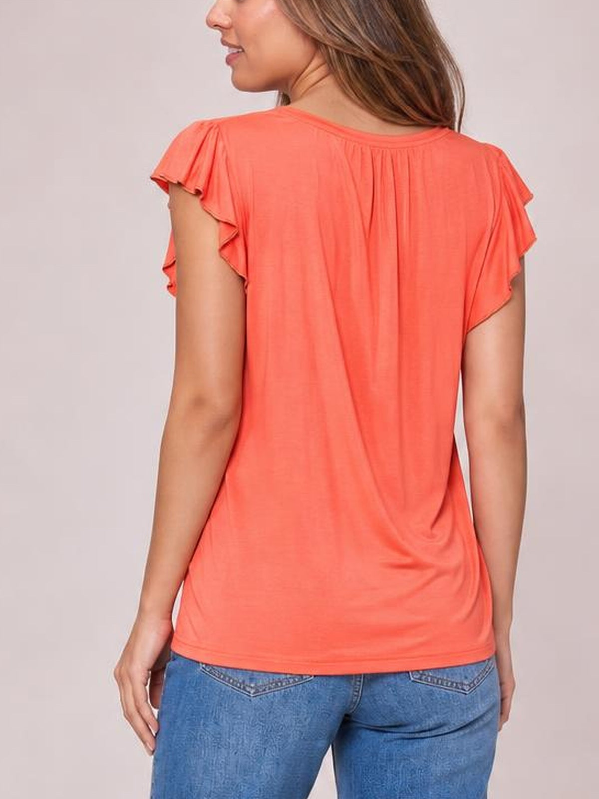 A model shown from behind wears a coral bamboo short-sleeve T-shirt with layered ruffled sleeves, a soft draped silhouette, and a straight hem.