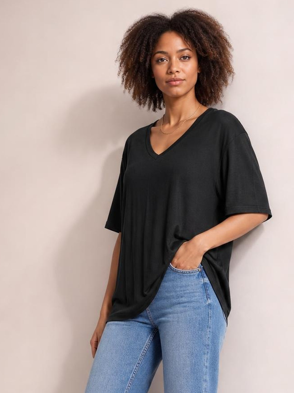 Model poses in a black Bamboo V-Neck Drop Shoulder T-Shirt with an oversized silhouette, short sleeves, and a relaxed draped hem.