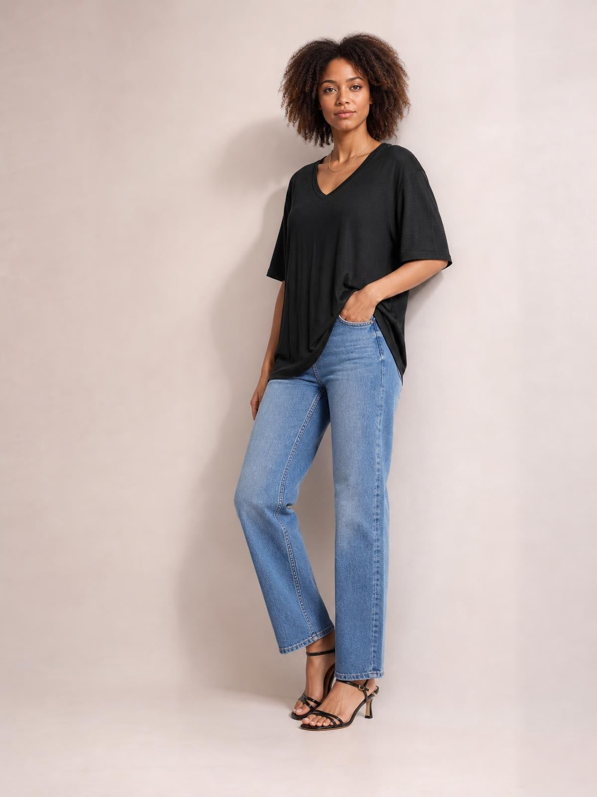 Model wearing a black bamboo V-neck drop shoulder T-shirt with an oversized silhouette, short sleeves, and a relaxed hem over light-wash jeans.