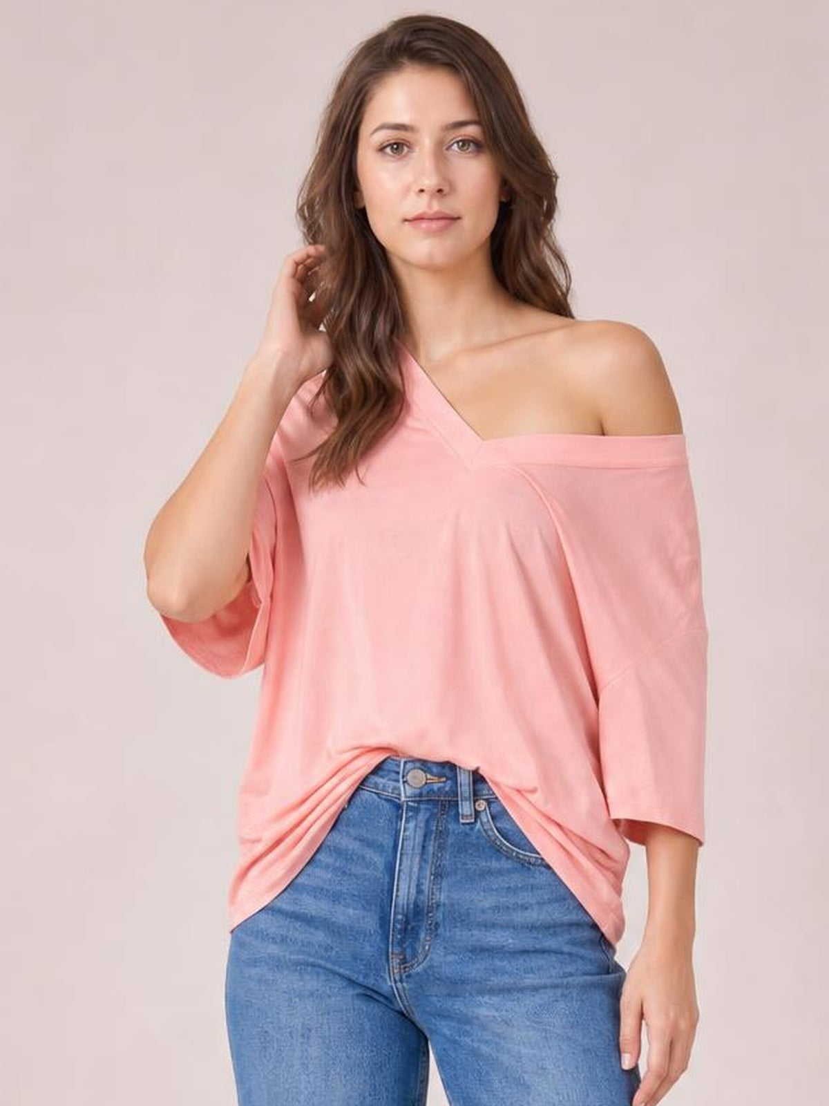 A model poses in a soft pink bamboo V-neck T-shirt with a relaxed drop-shoulder silhouette, loose elbow-length sleeves, and a casual front tuck into jeans.